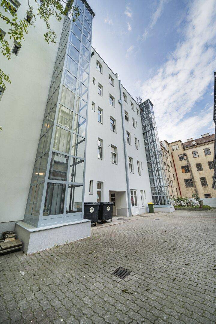 Außenansicht eines Wohngebäudes mit Glasaufzügen und gepflastertem Innenhof.