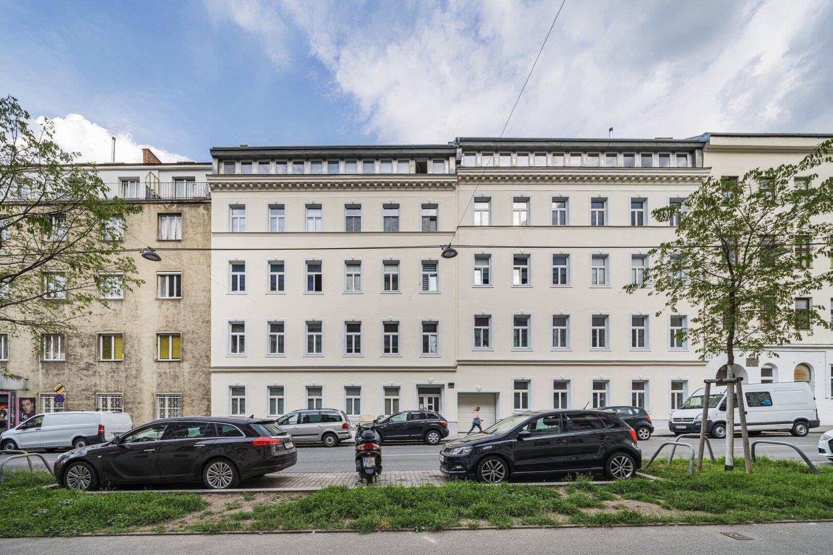 Straßenansicht eines klassischen Wohngebäudes mit vielen Fenstern und parkenden Autos.
