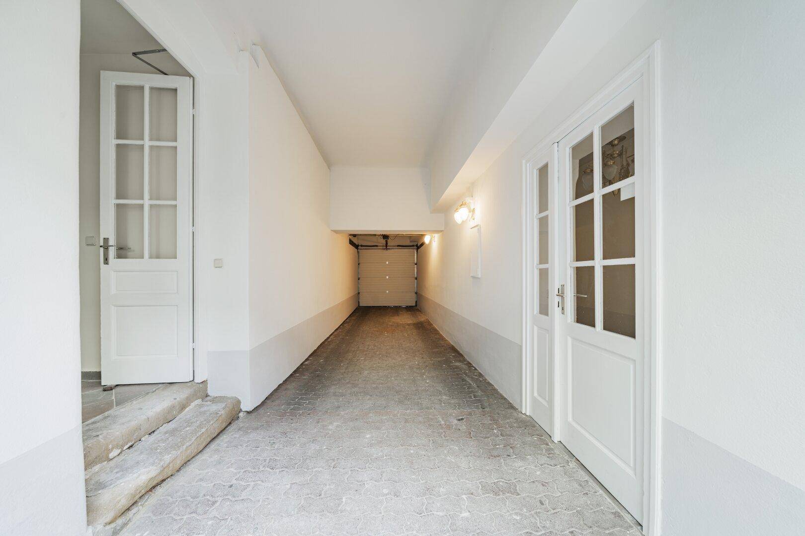 Einfahrt zu einer Garage mit weiß gestrichenen Wänden und einem Garagentor im Hintergrund.
