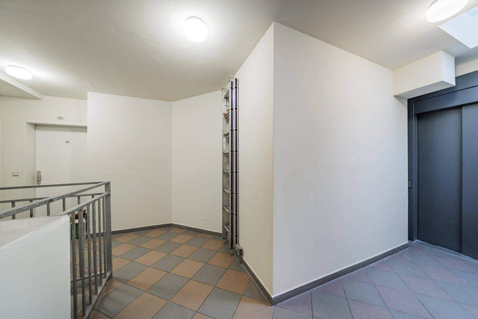 Heller Flur mit Aufzug und Treppenhaus, mit gemustertem Fliesenboden.