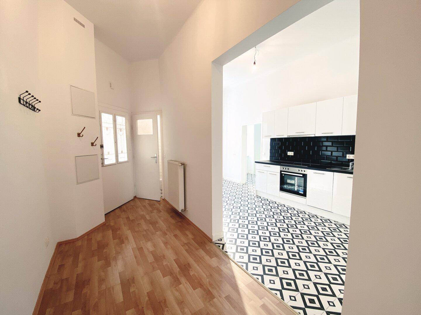 Eingangsbereich mit Garderobe und Blick auf die moderne Küche mit Fliesenboden.