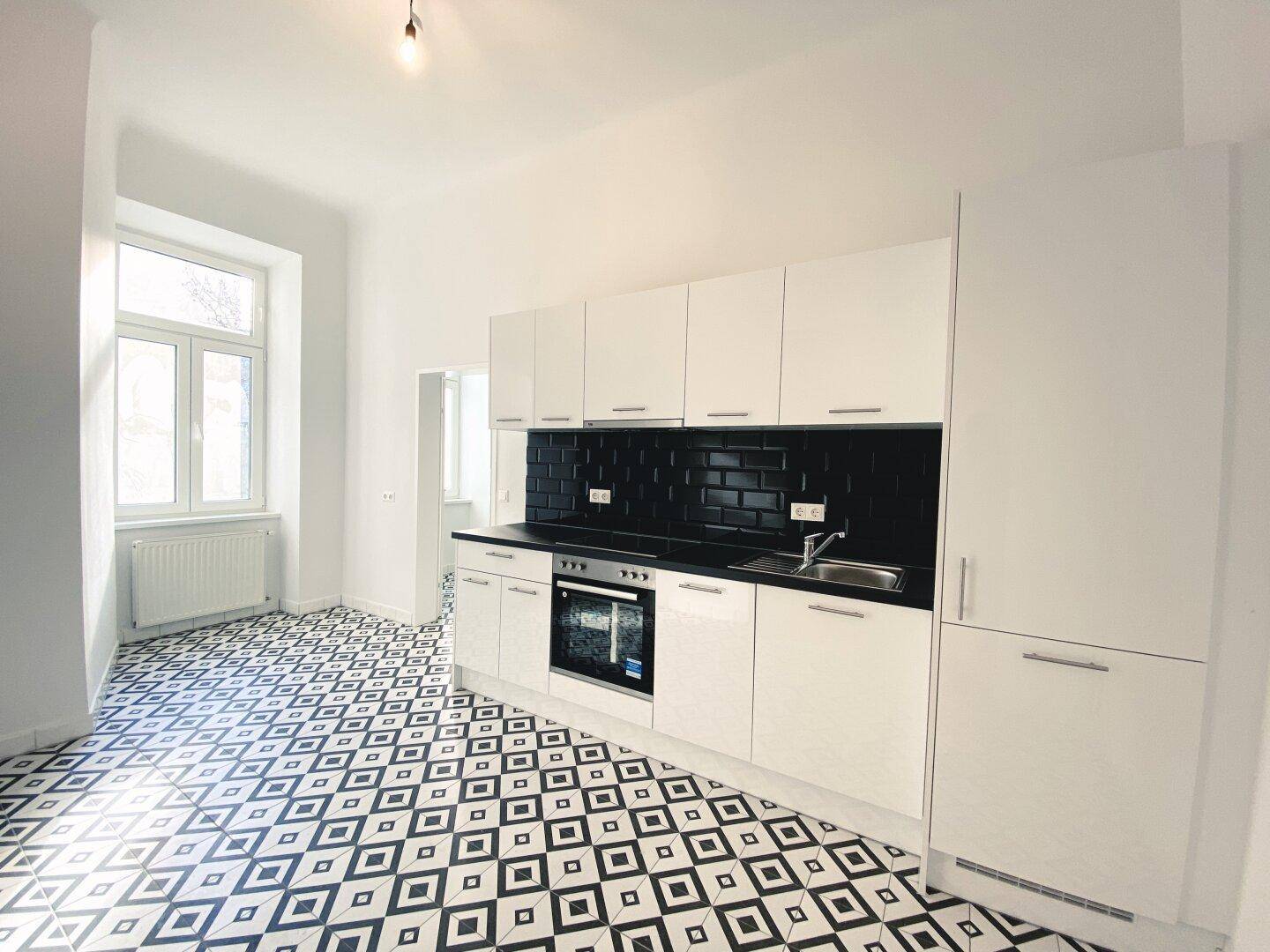 Moderne Einbauküche mit weißen Schränken, schwarzem Fliesenspiegel und stilvollem Fliesenboden.