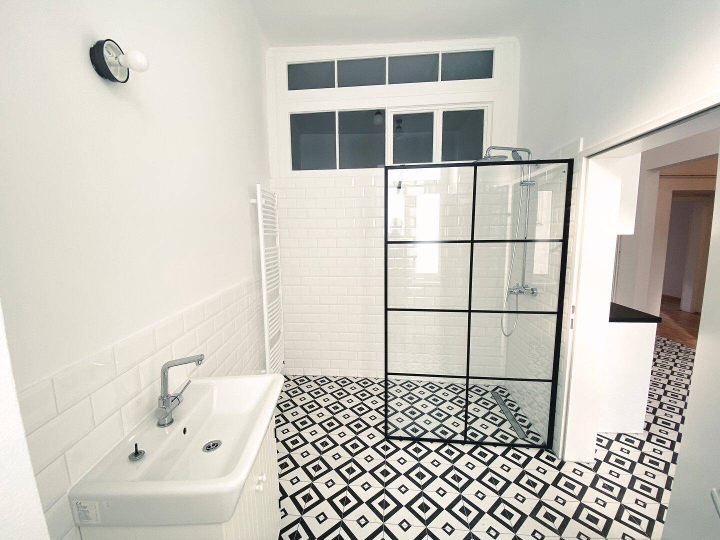 Badezimmer mit Fenster, moderner Dusche und Waschbecken, verbunden mit dem Küchenbereich.