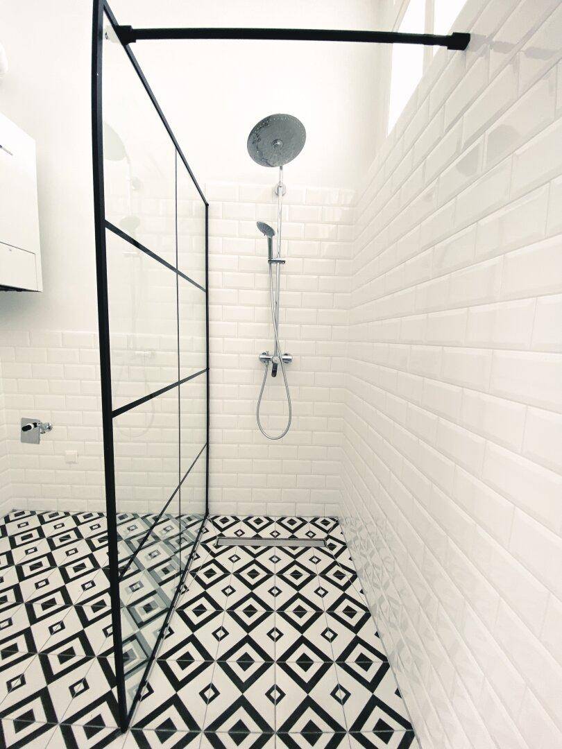 Detaillierte Ansicht der modernen begehbaren Dusche mit Regenduschkopf und stilvollen Bodenfliesen.