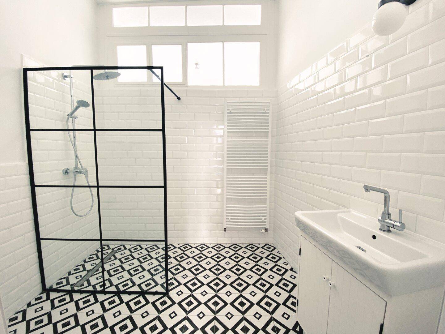 Modernes Badezimmer mit begehbarer Dusche, auffälligen Fliesen und Fenster für Tageslicht.