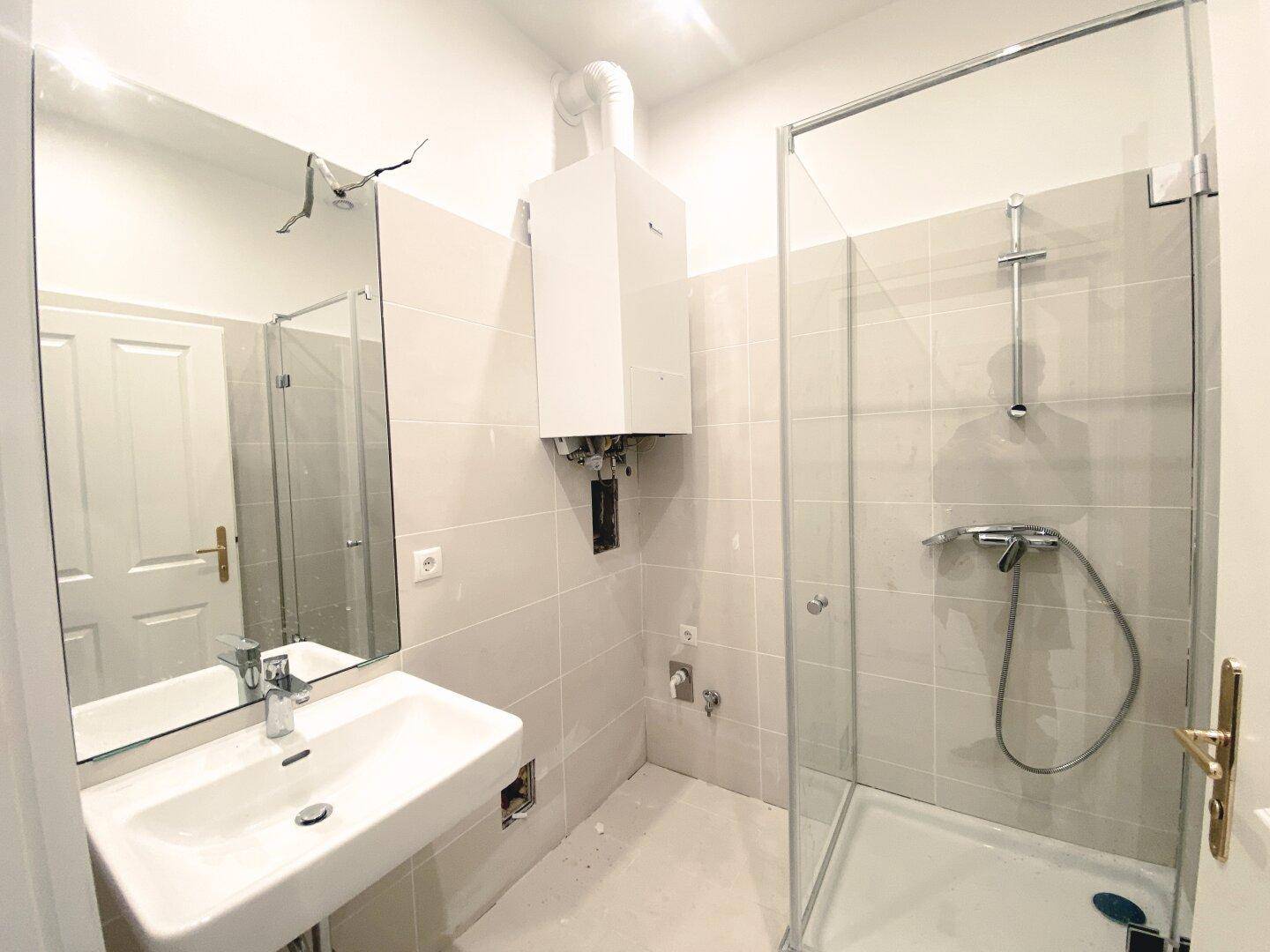Modernes Badezimmer mit Duschkabine, Waschbecken und Wandfliesen in hellem Grau.