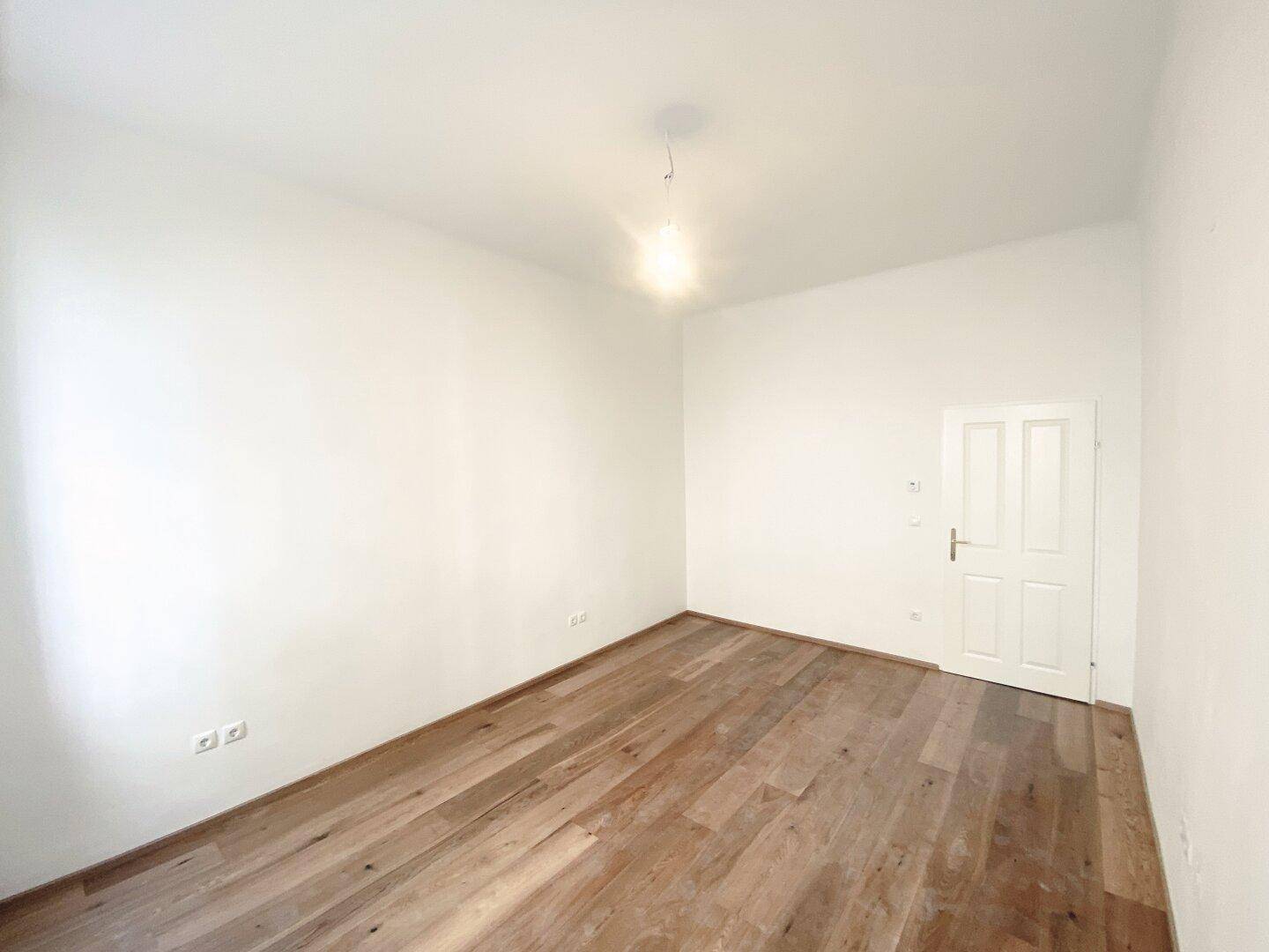 Leeres Zimmer mit Holzboden und einer Tür, bietet vielseitige Nutzungsmöglichkeiten.