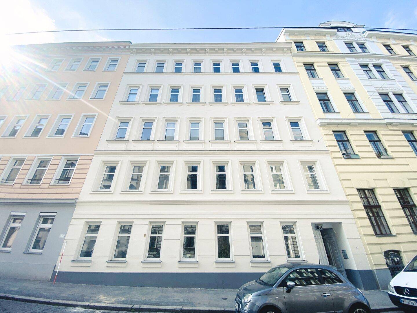 Klassische Fassade eines Mehrfamilienhauses mit vielen Fenstern und Sonnenschein.