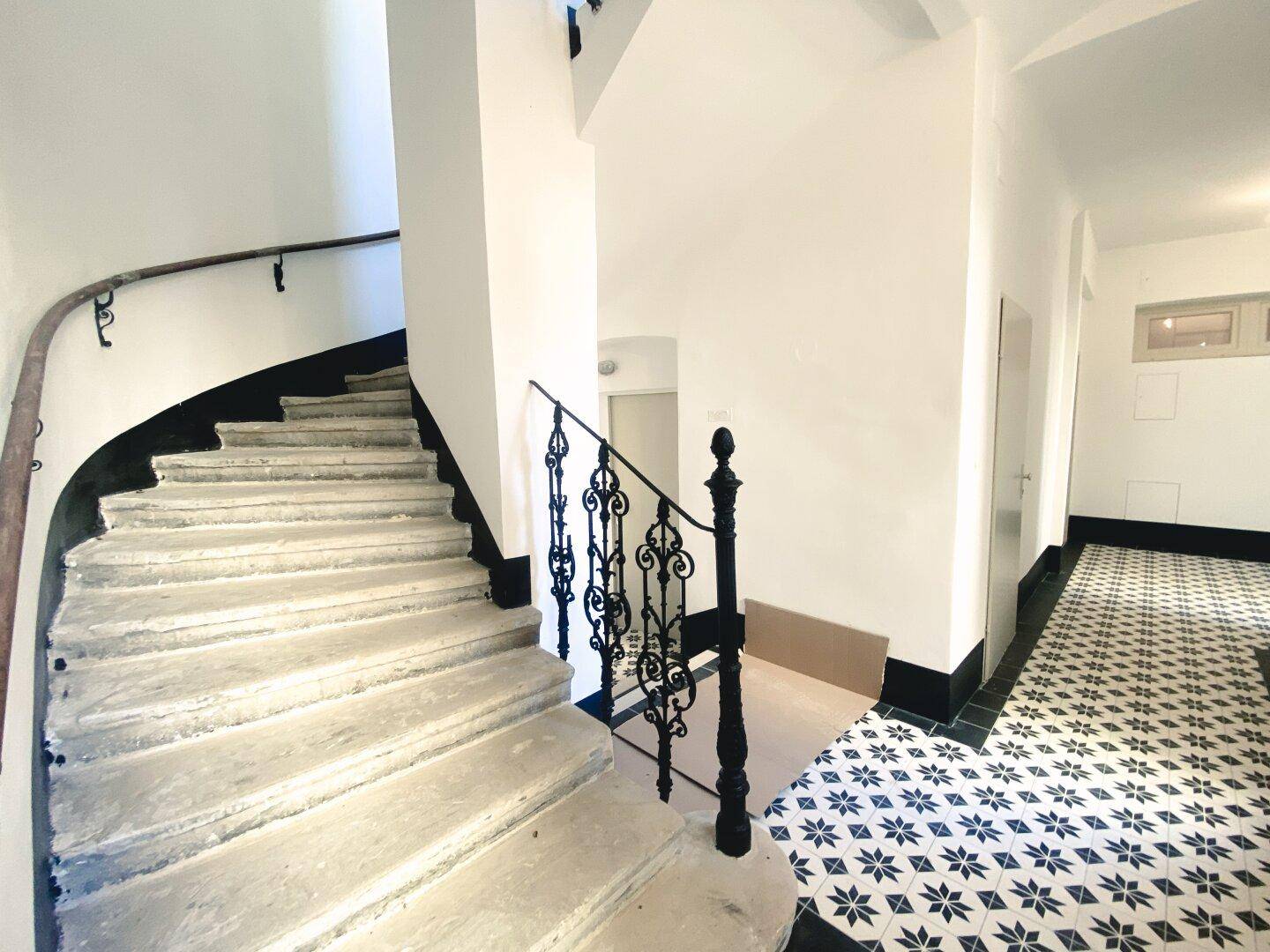 Historisches Treppenhaus mit schmiedeeisernem Geländer und gemustertem Fliesenboden im Eingangsbereich.