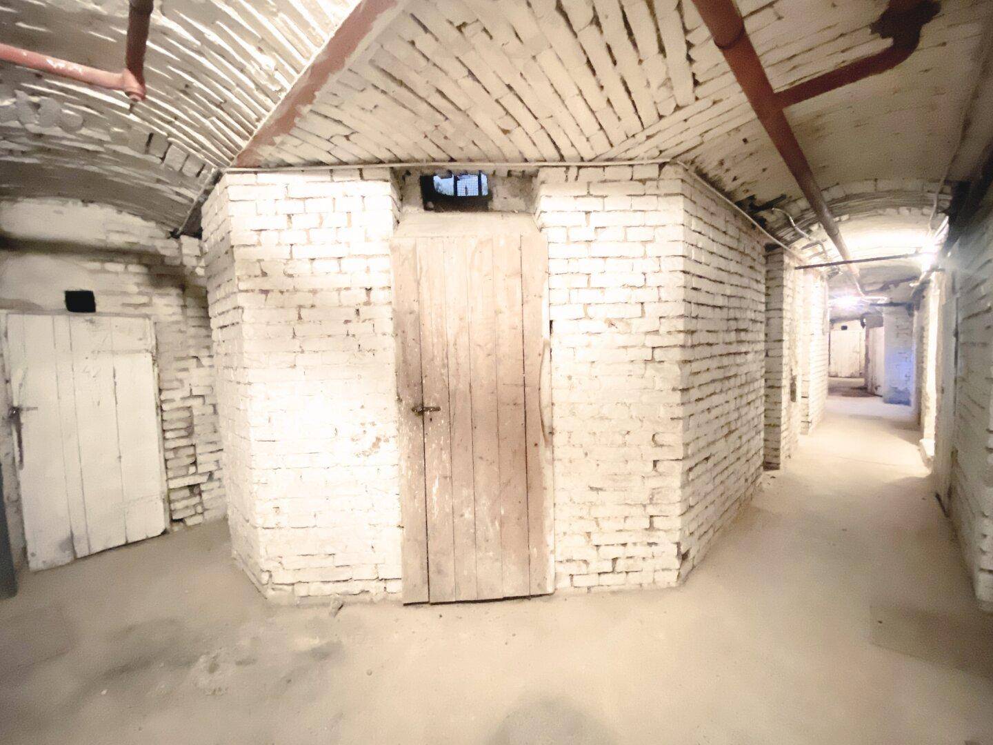 Rustikaler Kellerraum mit Ziegelwänden und Holztüren, bietet zusätzlichen Stauraum.