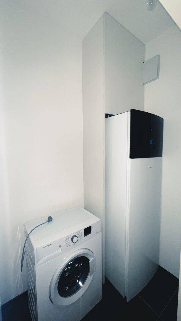 Praktischer Hauswirtschaftsraum mit Waschmaschine und moderner Wärmepumpe für effiziente Energieversorgung.