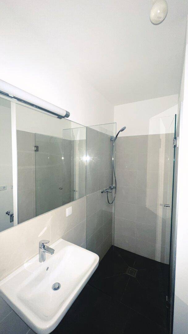 Helles Badezimmer mit Duschkabine, Waschbecken und großem Spiegel, in modernem Design.