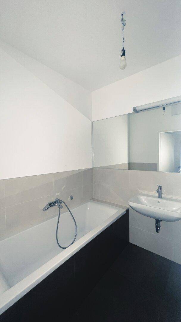 Modernes Badezimmer mit Badewanne, Waschbecken und großem Spiegel, in neutralen Farben gehalten.