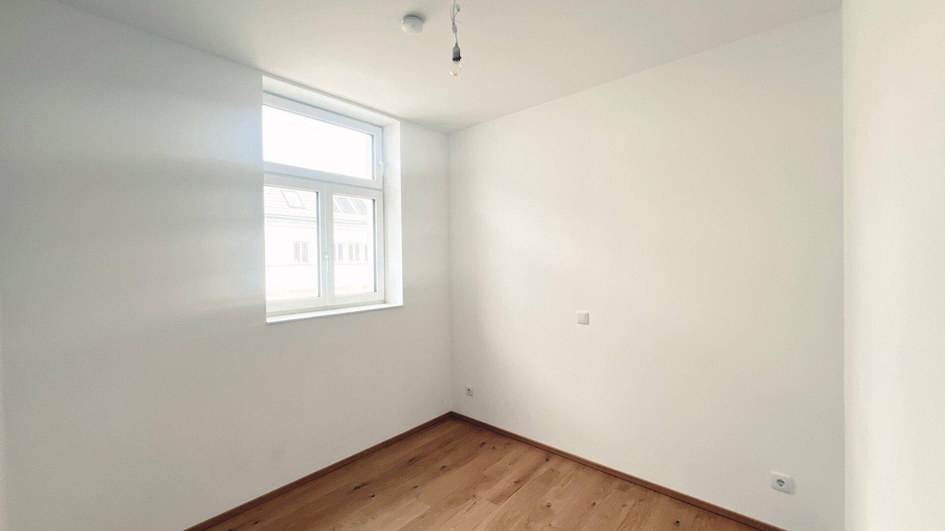 Unmöbliertes Zimmer mit großem Fenster und Holzboden, ideal als Schlaf- oder Arbeitszimmer.