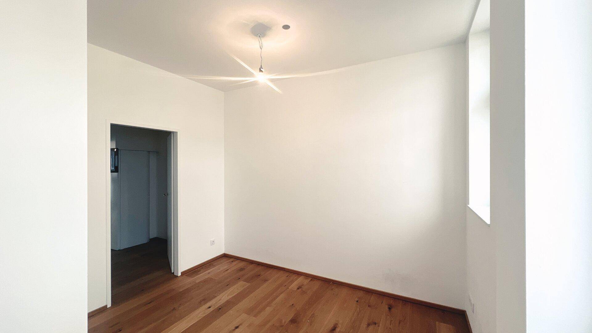 Helles Zimmer mit Parkettboden und einem Fenster, bereit für die Möblierung.