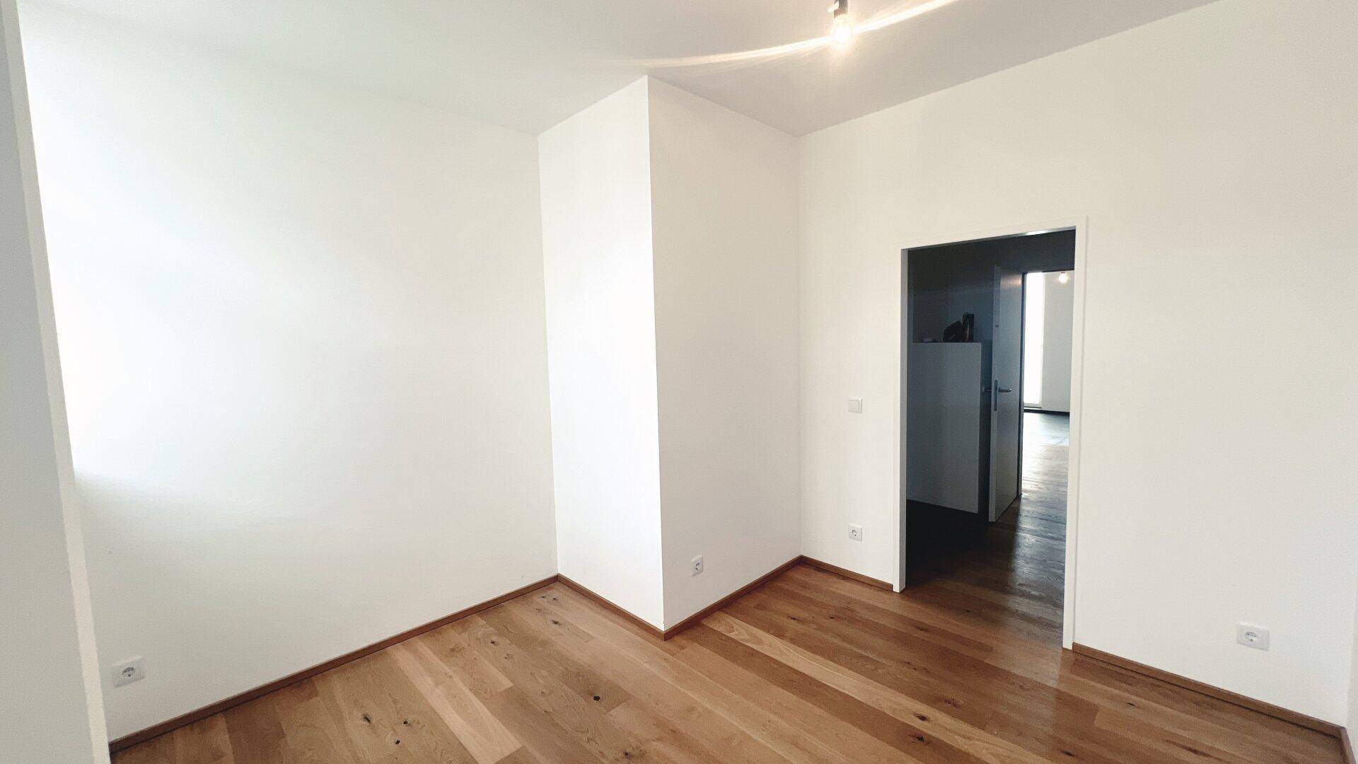 Leeres Zimmer mit hellem Parkettboden und weiß gestrichenen Wänden, bereit zur Einrichtung.