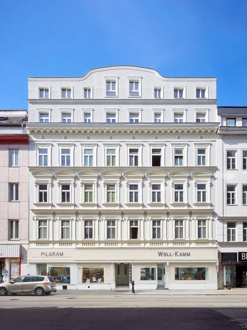 Historische Fassade eines eleganten Gebäudes mit Geschäften im Erdgeschoss und vielen Fenstern.