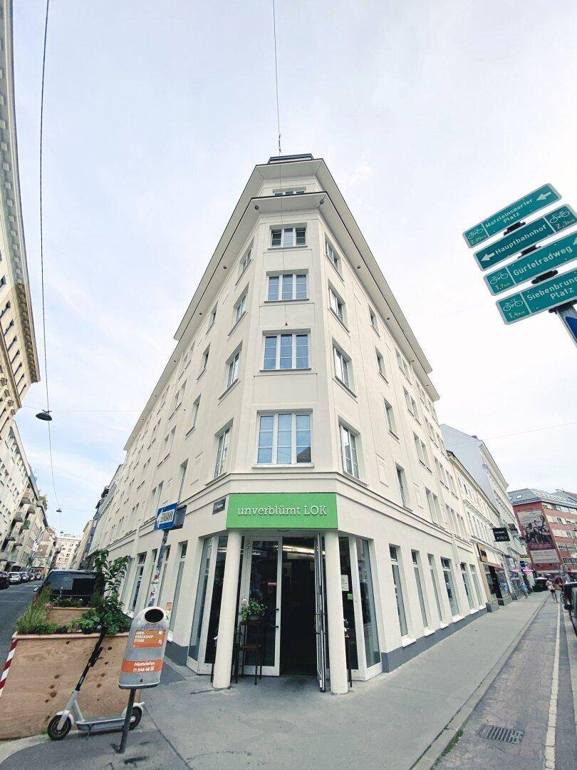 Eckgebäude mit moderner Architektur und Geschäftsräumen im Erdgeschoss an einer Stadtstraße.