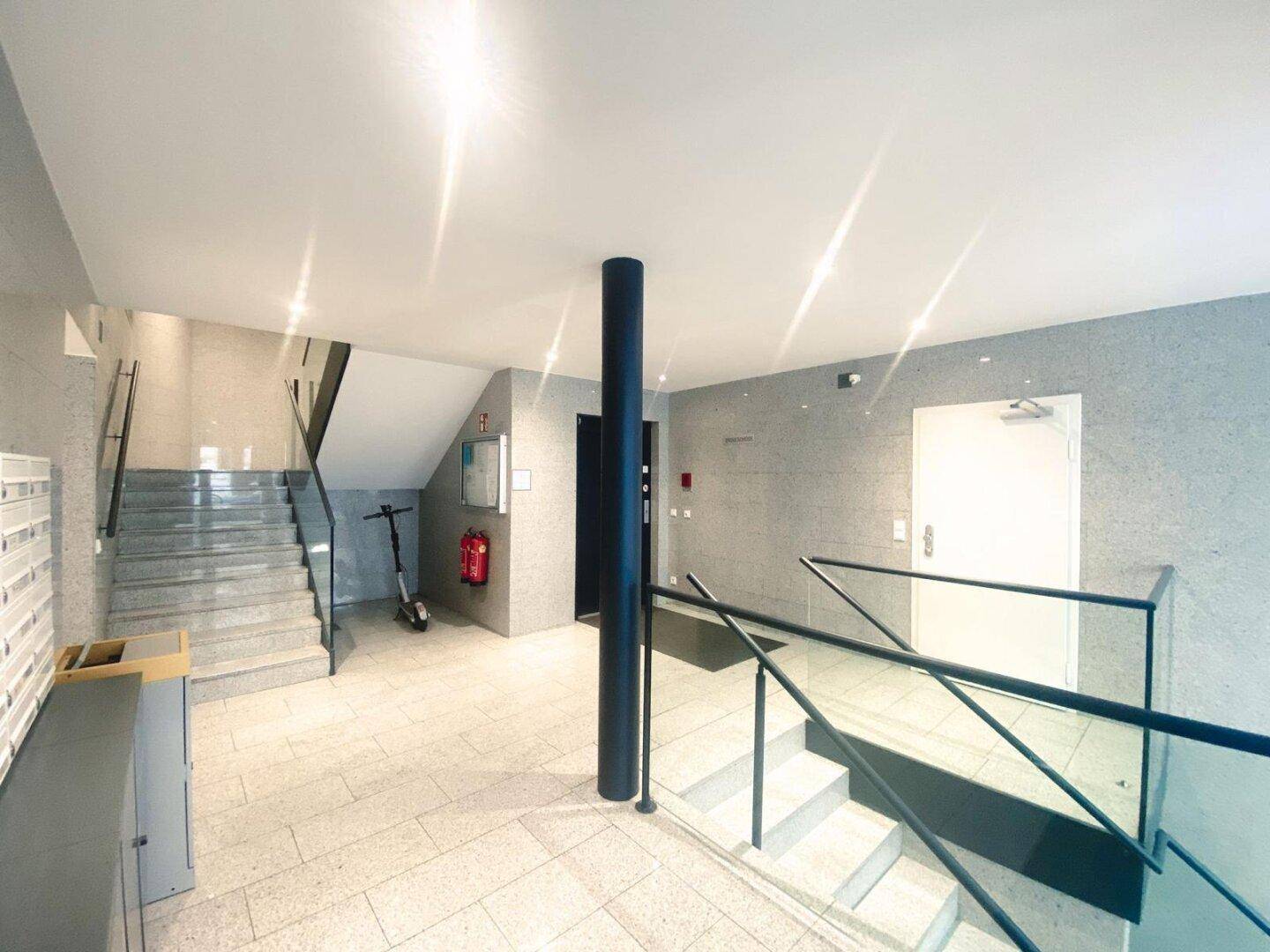 Heller Eingangsbereich mit Granitboden, Treppe und Glasgeländer, der zu den Wohnungen führt.