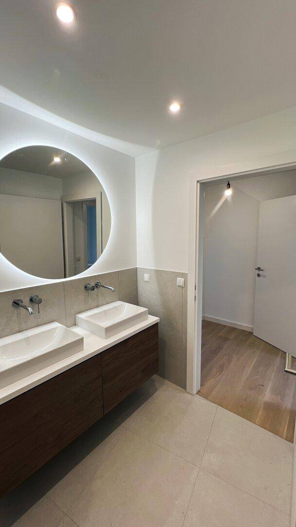 Modernes Badezimmer mit Doppelwaschbecken, beleuchtetem Spiegel und Dusche.