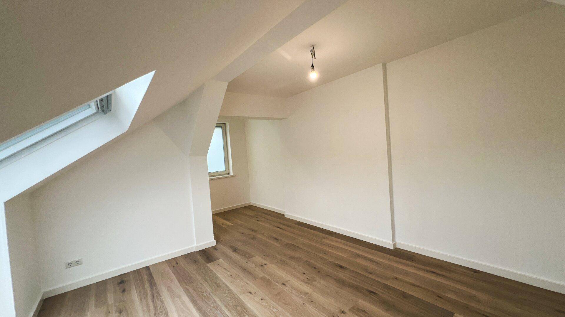 Unmöbliertes Schlafzimmer im Dachgeschoss mit Holzboden und einem Fenster.