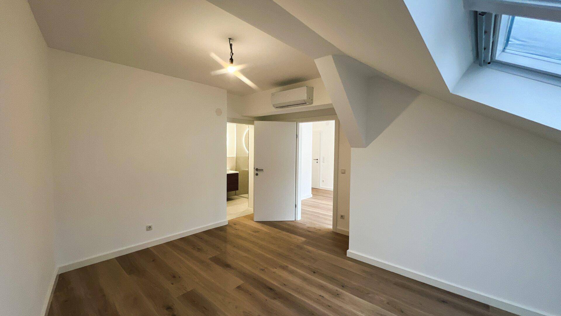 Unmöbliertes Schlafzimmer mit Holzboden und Zugang zu einem modernen Badezimmer.