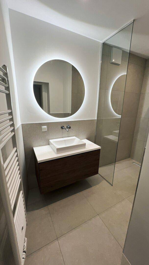 Modernes Badezimmer mit beleuchtetem Spiegel, Einzelwaschbecken und beheiztem Handtuchhalter.