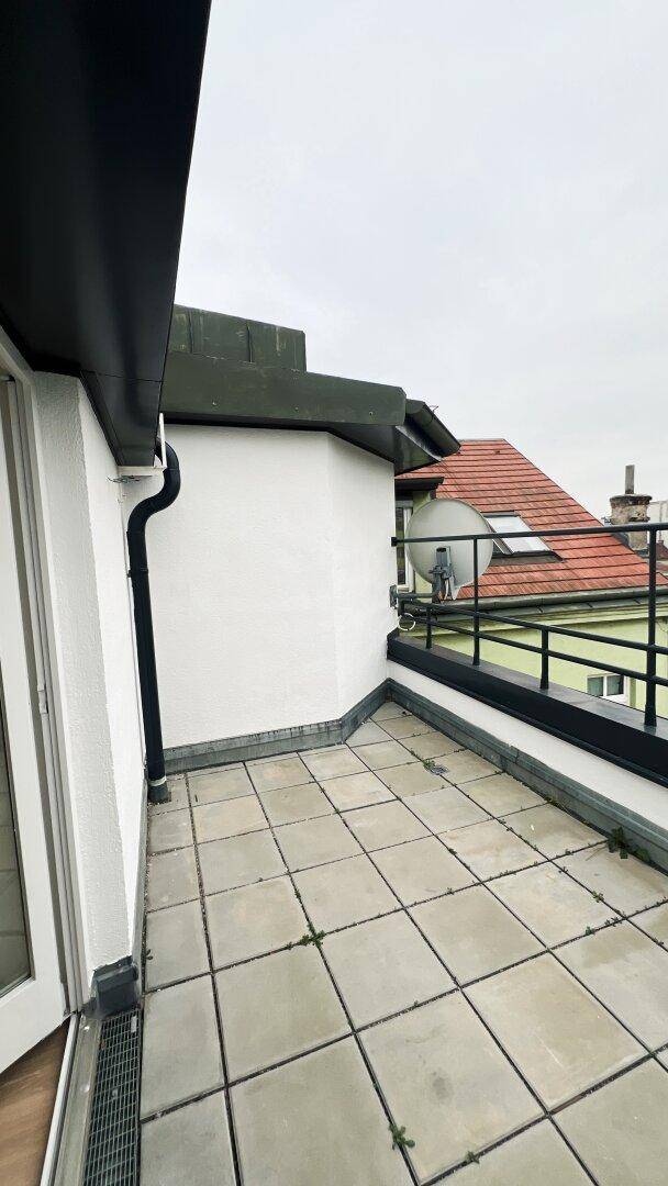 Dachterrasse mit Fliesenboden und Blick auf die Dächer der Nachbargebäude.