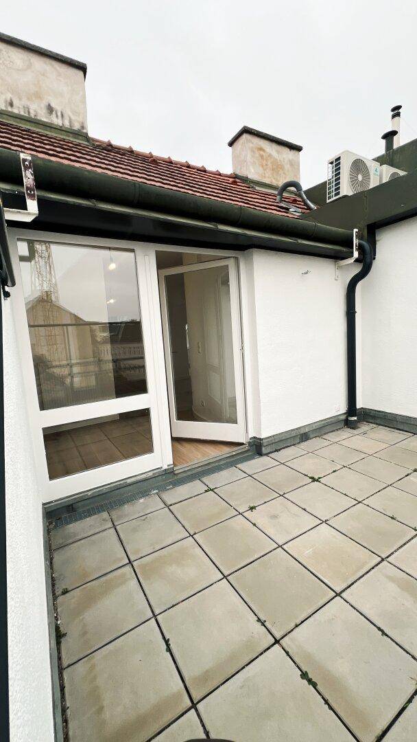 Dachterrasse mit Fliesenboden und Zugang zum Innenbereich durch eine Glastür.