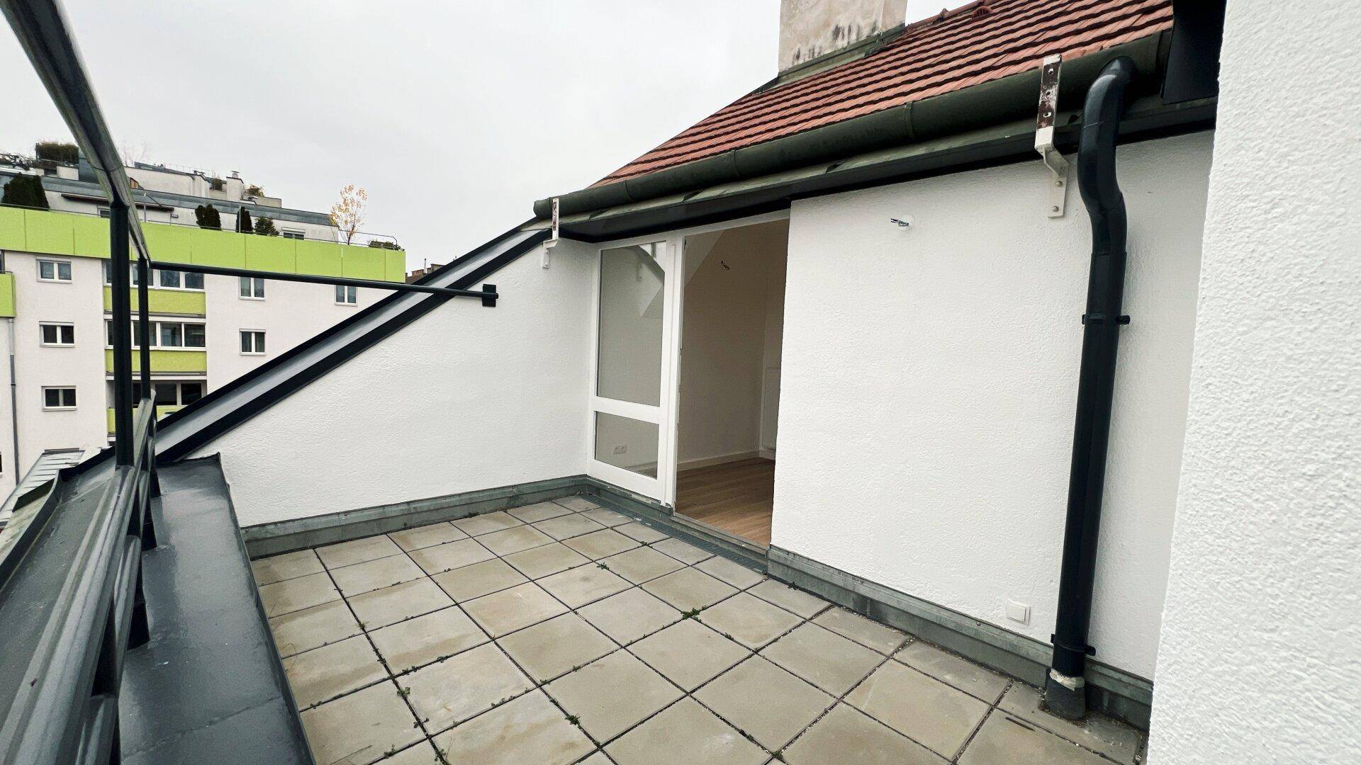 Dachterrasse mit Fliesenboden und Blick auf die umliegenden Gebäude und Dächer.