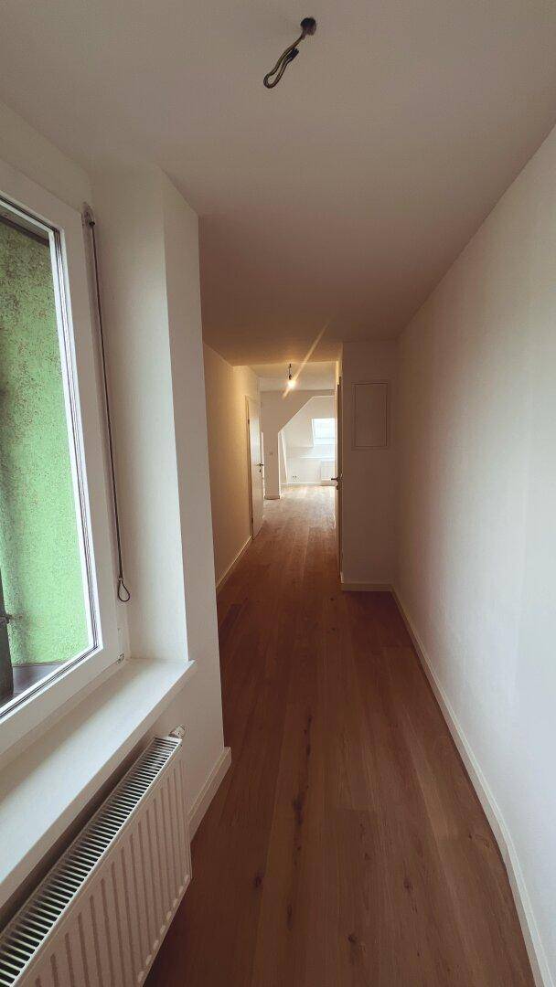 Heller Flur mit Holzboden und Fenster, der zu weiteren Räumen führt.
