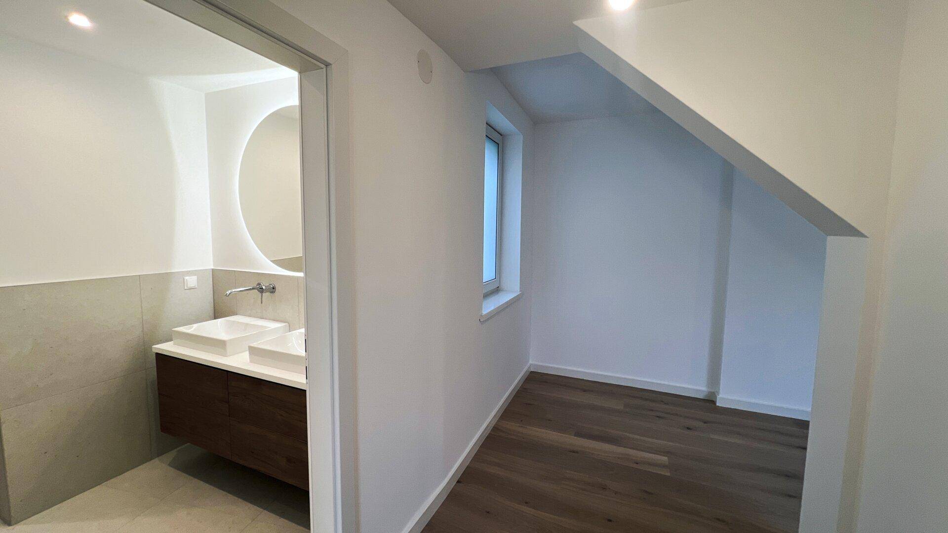 Helles Schlafzimmer mit Holzboden und Zugang zu einem modernen Badezimmer.