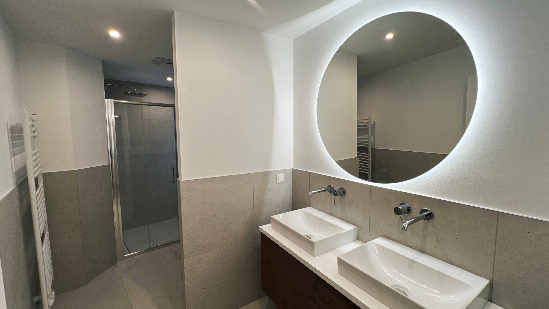 Modernes Badezimmer mit Doppelwaschbecken, beleuchtetem Spiegel und Dusche.