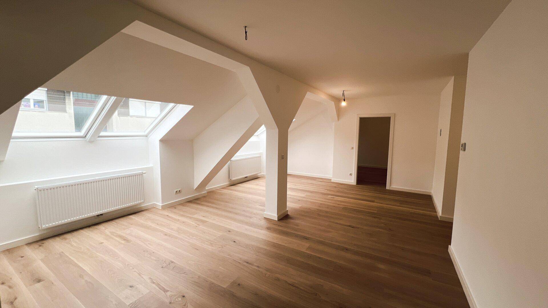 Geräumiger, unmöblierter Wohnbereich im Dachgeschoss mit Holzboden und Dachfenstern.
