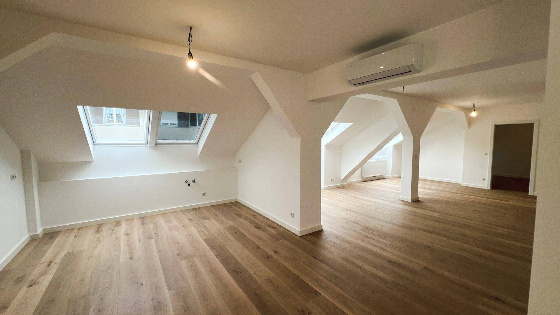 Heller, unmöblierter Wohnbereich im Dachgeschoss mit Holzboden und mehreren Dachfenstern.