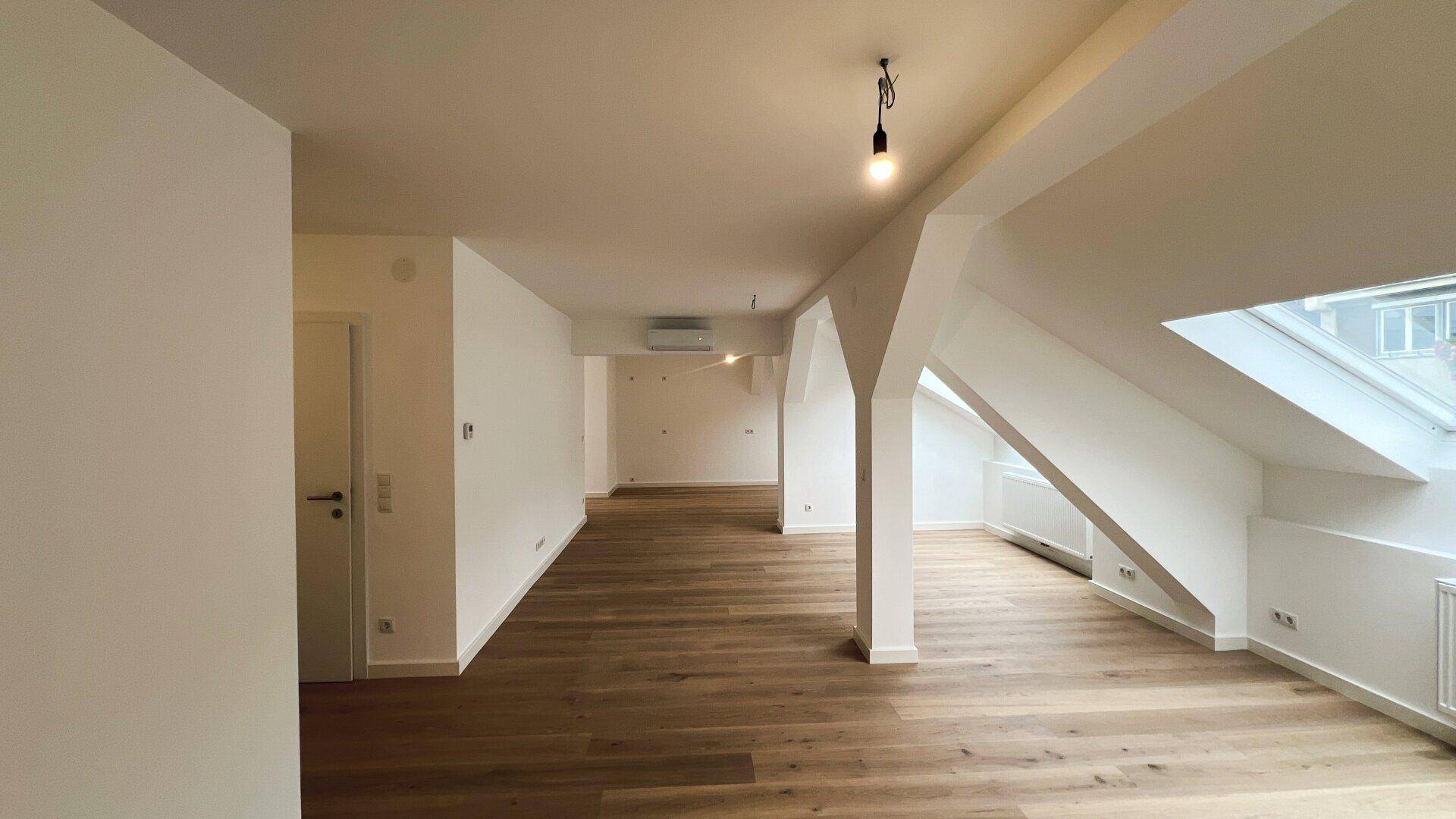 Langer, heller Wohnbereich im Dachgeschoss mit Holzboden und Dachfenstern.