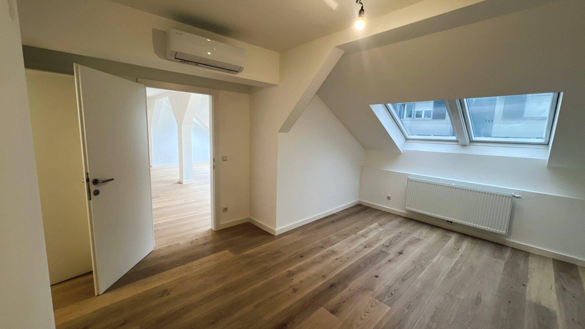 Helles Schlafzimmer im Dachgeschoss mit Holzboden, Dachfenster und Klimaanlage.