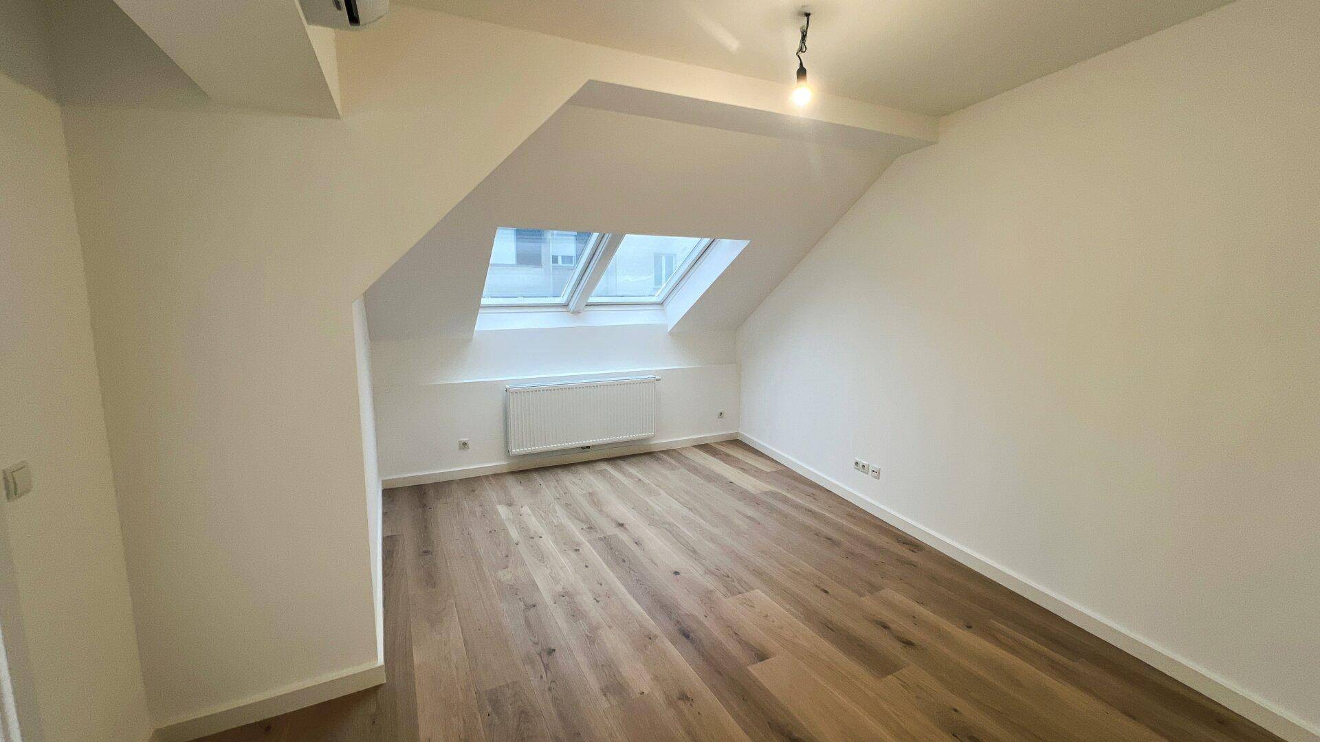 Helles, unmöbliertes Schlafzimmer im Dachgeschoss mit Holzboden und Dachfenster.