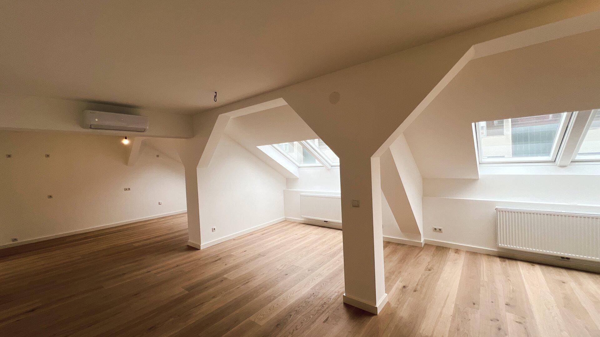 Heller, unmöblierter Wohnbereich im Dachgeschoss mit Holzboden und mehreren Dachfenstern.