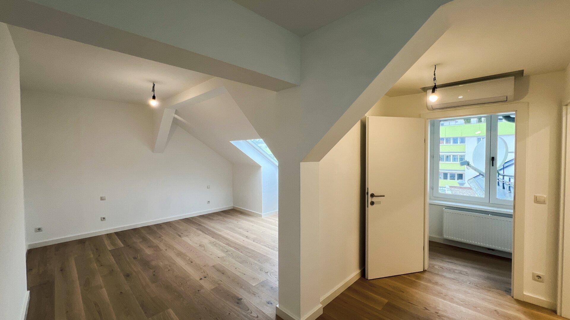 Unmöbliertes Schlafzimmer im Dachgeschoss mit Holzboden, Dachfenster und Klimaanlage.