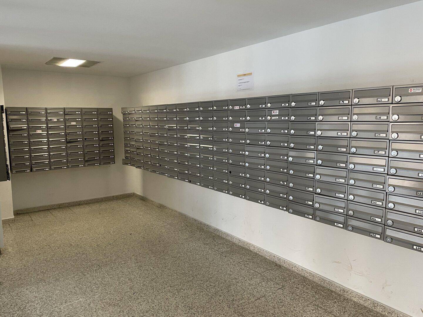 Langer Flur mit zahlreichen Briefkästen an den Wänden und Fliesenboden im Eingangsbereich.