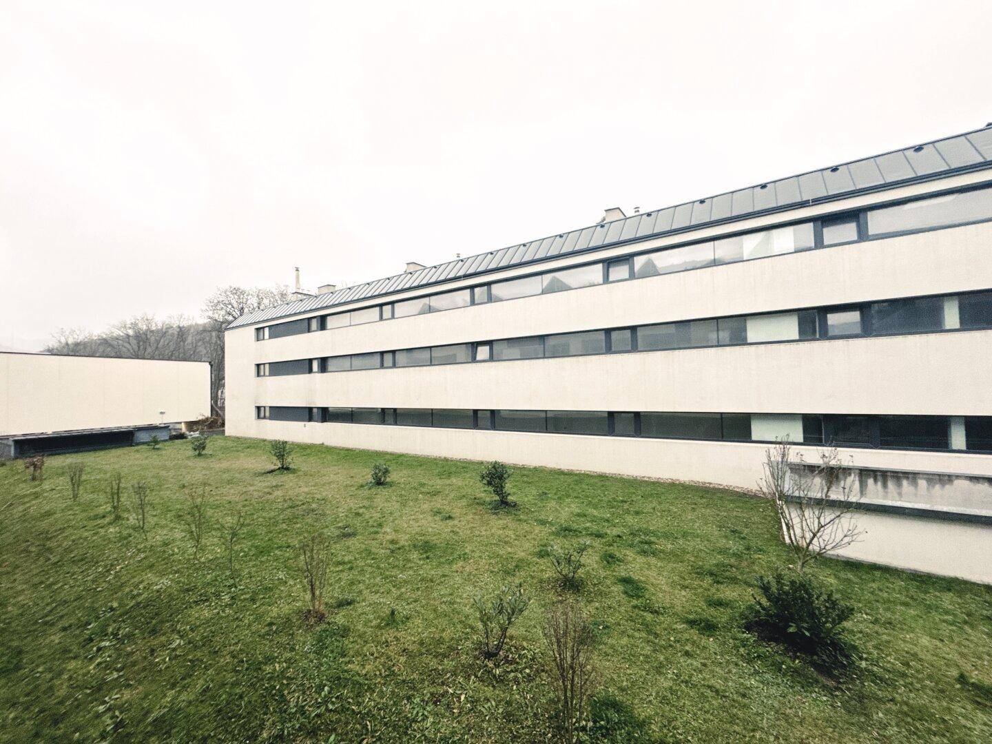 Moderne Gebäudefassade mit langen Fensterreihen und einer grünen Rasenfläche im Vordergrund.