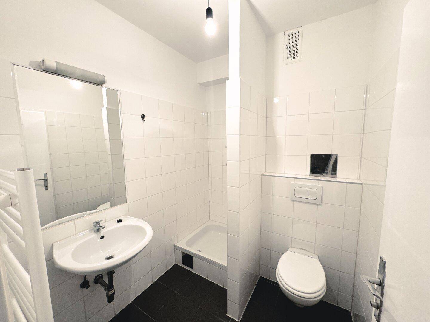 Modernes Badezimmer mit weißen Fliesen, Dusche, Waschbecken und wandhängendem WC.
