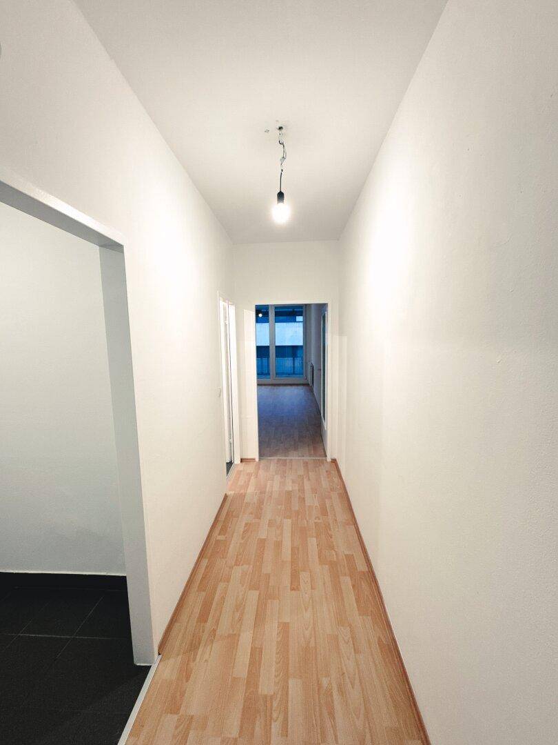 Heller Flur mit Laminatboden, der zu einem weiteren Zimmer mit Balkonzugang führt.