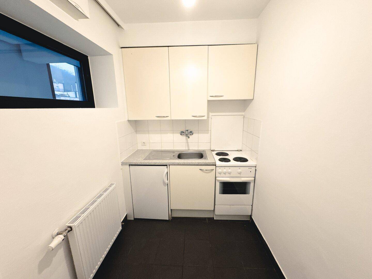 Kleine Küchenzeile mit einfachen Schränken, Spüle, Herd und Kühlschrank.