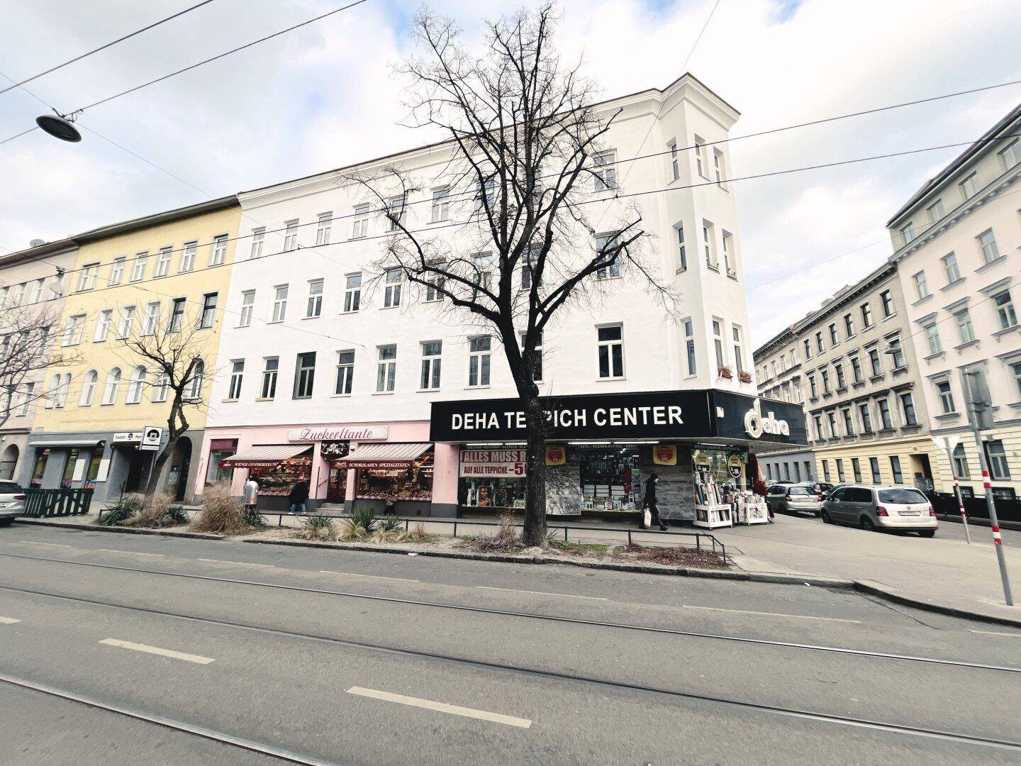 Eckgebäude mit weißer Fassade und Geschäften im Erdgeschoss an einer städtischen Kreuzung.