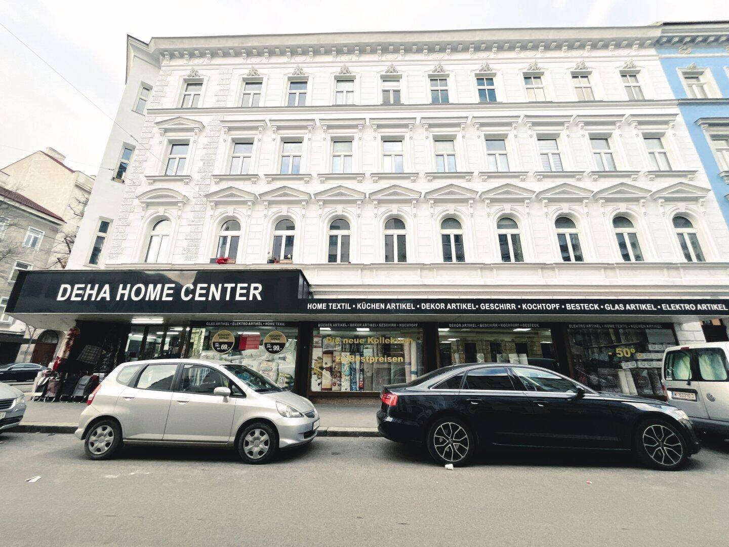 Historisches Gebäude mit weißer Fassade und Geschäften im Erdgeschoss an einer belebten Straße.