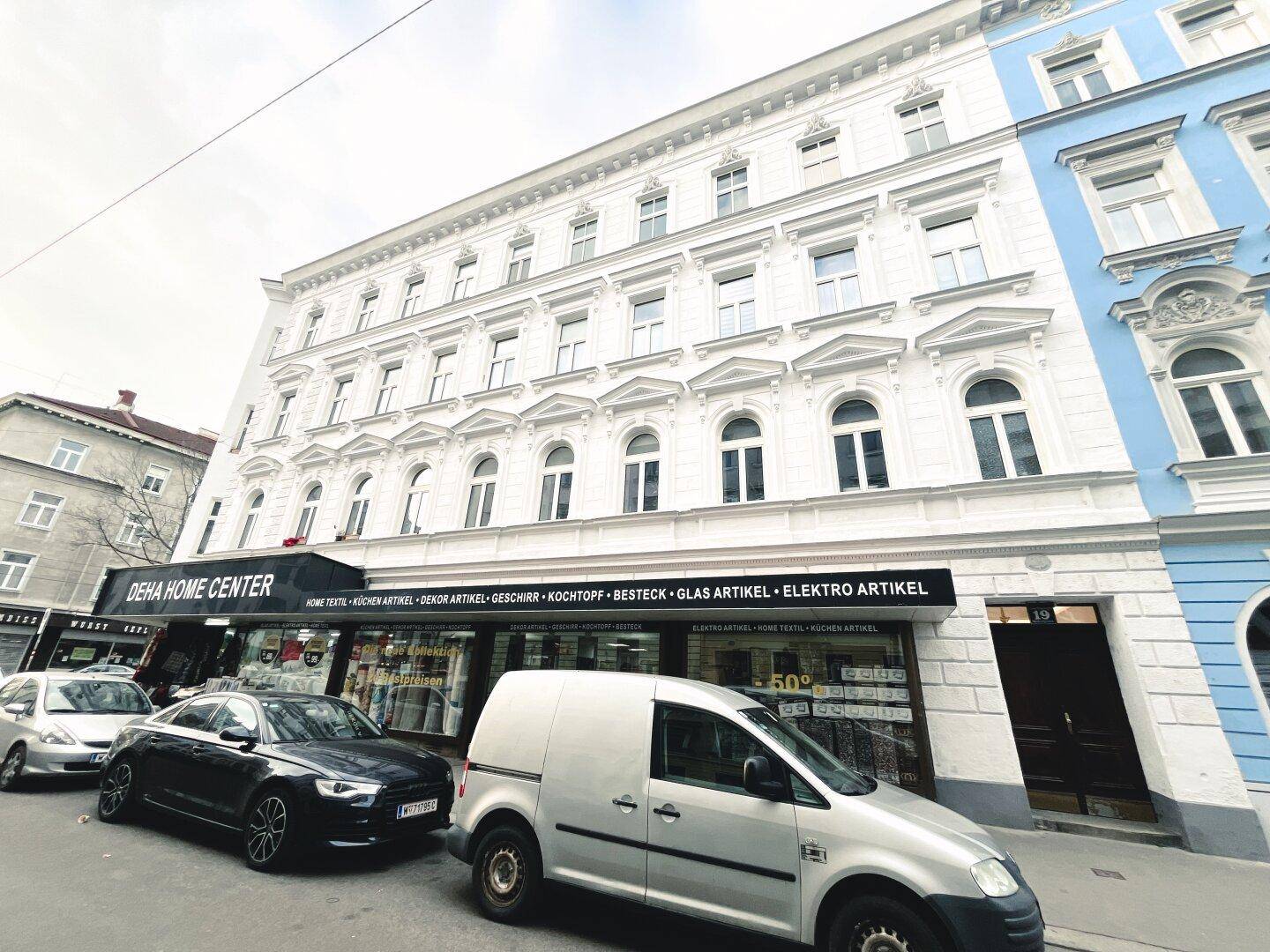 Historisches Gebäude mit weißer Fassade und Geschäften im Erdgeschoss an einer Stadtstraße.