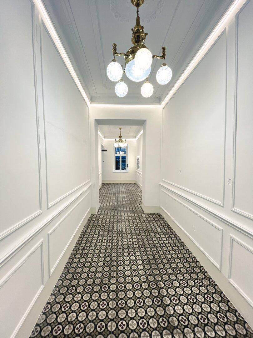 Langer, eleganter Hausflur mit gemusterten Fliesen, Stuckelementen und klassischer Deckenleuchte.