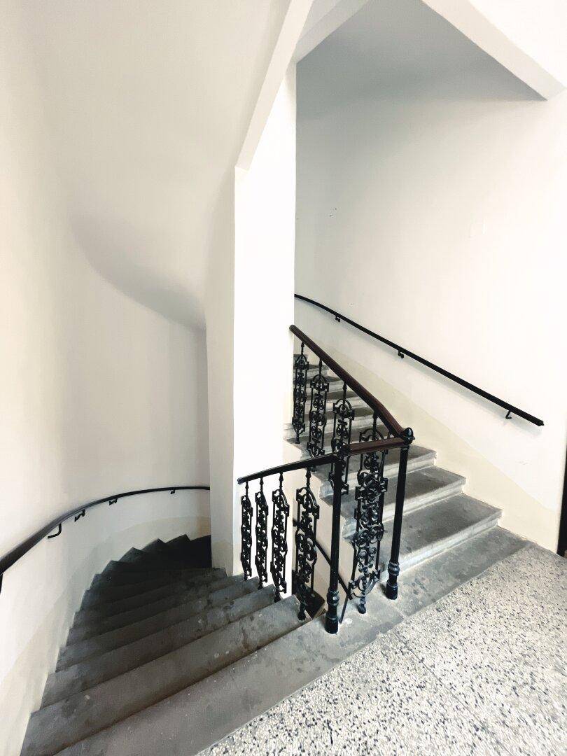 Historisches Treppenhaus mit Steinstufen und schmiedeeisernem Geländer in einem Altbau.